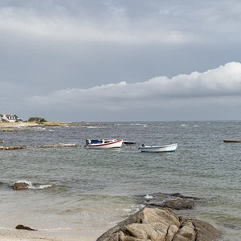 Petits bateaux au mouillage devant la côte de Penmarc’h sous un ciel nuageux en Bretagne
