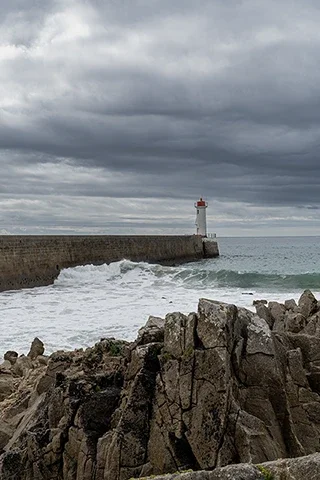 Le môle et le phare du Raoulic à Audierne sous un ciel chargé et face à une mer agitée.