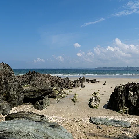 Rochers sombres et plage de sable clair sur la plage des Curés à Plestin-les-Grèves en Bretagne sous un ciel lumineux.